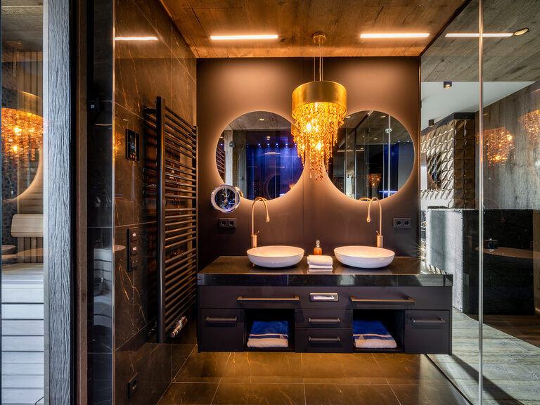 Badezimmer mit runden Spiegeln an dunklen Wänden über den Waschbecken und Kronleuchter