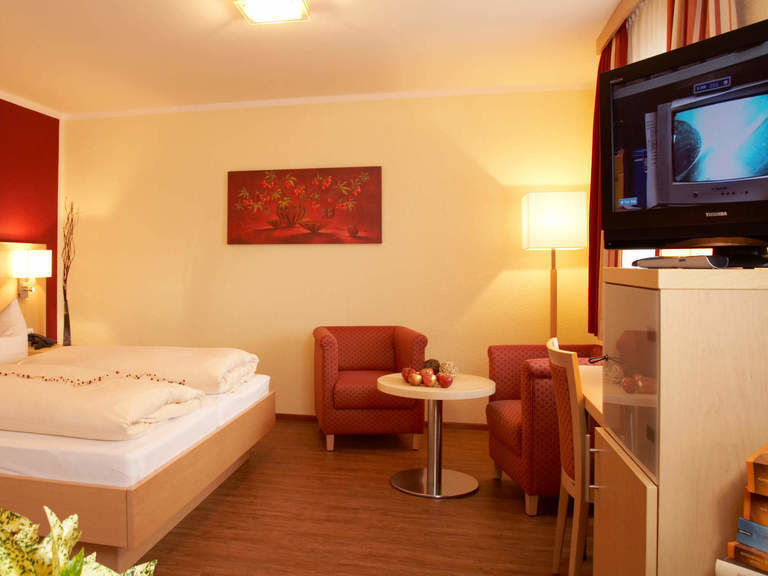 Gemütliches Hotelzimmer, mit Blütenblättern dekoriertem Doppelbett, Sitzecke und TV