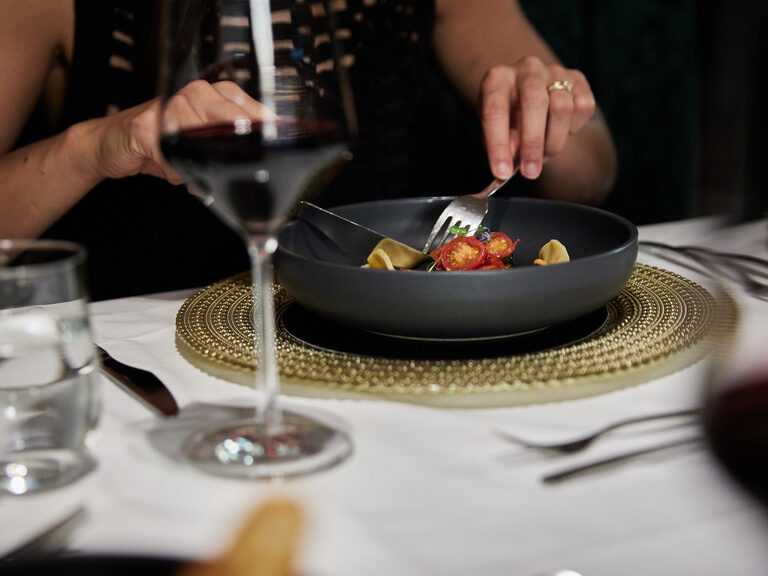 Nahaufnahme von Gericht auf schwarzem Teller, das von Gast am Tisch mit Besteck zerteilt wird
