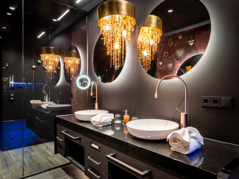 Modernes, dunkles Bad mit runden Spiegeln und Waschbecken, leuchtendem Kosmetikspiegel und Kronleuchter