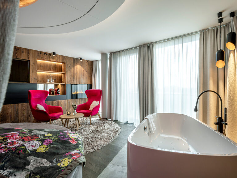 Modernes Luxuszimmer mit rundem Bett, zwei Samt-Sessel und Badewanne im Hüttenhof