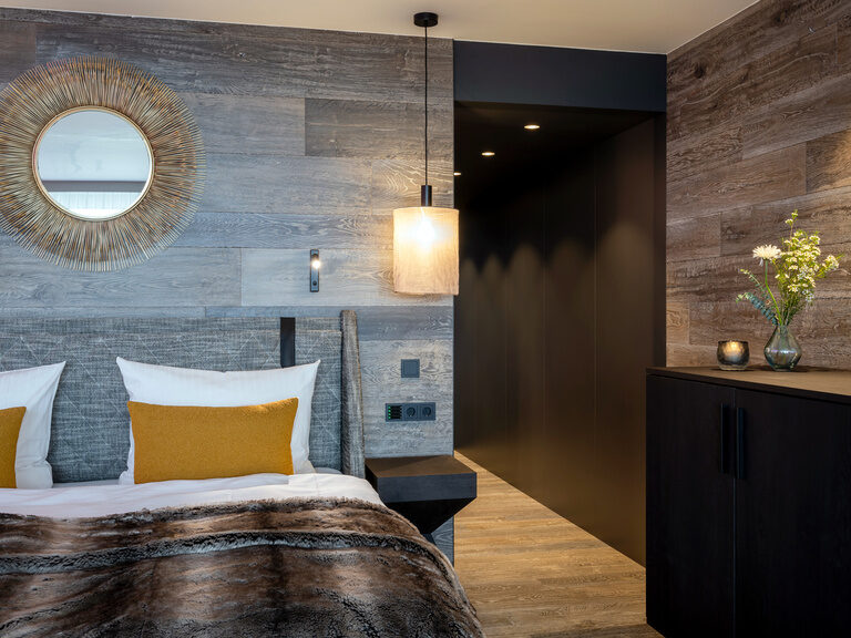Modernes Doppelbett in Hotelzimmer neben dunklem Regal an der Holzwand, auf dem Blumenvase steht