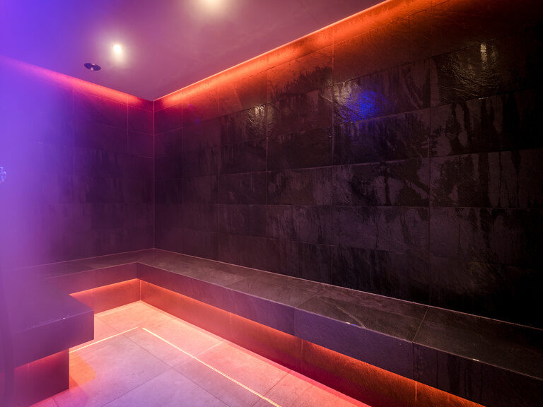 Modern gestalteter Raum mit Sitzbank für Aroma-Dampfbad, beleuchtet in warmen Rottönen