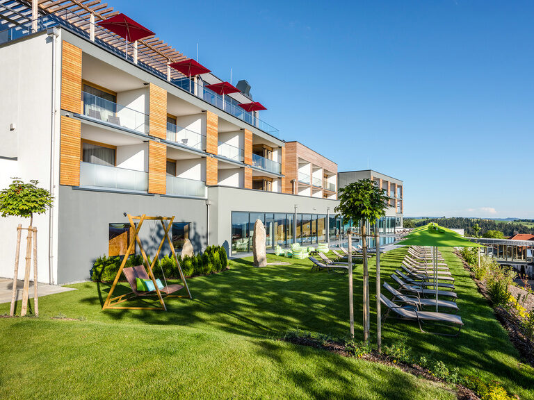Außenaufnahme Hotel Hüttenhof mit Liegen auf Wiese und Außenpool an sonnigem Tag