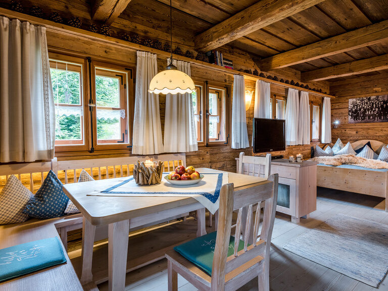 Badewanne, Sitzecke und Flachbild-TV in eleganter Suite im Luxushotel Hüttenhof Stilvolle Suite mit Sitzbereich, TV an Holzwand, frei stehender Badewanne und Balkon mit Liege