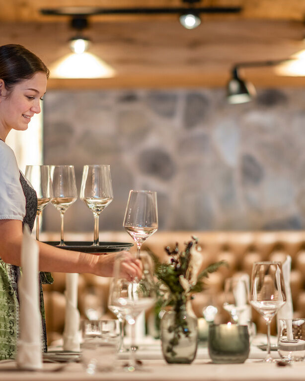 Bedienung in Dirndl stellt eines der Weingläser von Ihrem Tablet auf Tisch in modernem Restaurant
