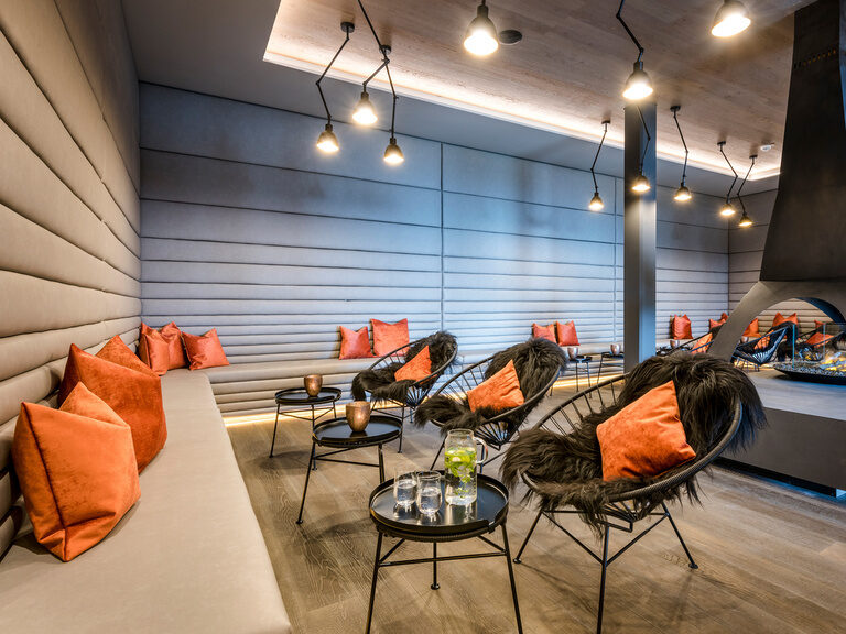 Beleuchteter, moderner Aufenthaltsraum mit offenem Kamin, umrandet von grauer Lounge