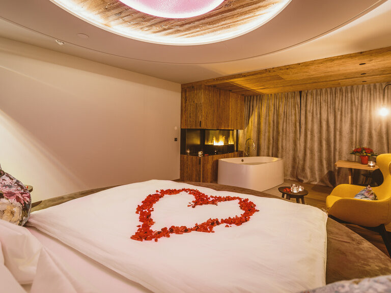 Romantisch dekoriertes, Luxus-Zimmer mit Kamin und Badewanne, Herz aus Rosenblättern auf Bett