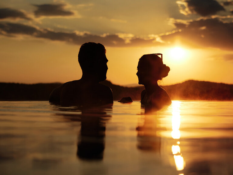 Bett in Zimmer vom Wellnesshotel Hüttenhof, mit Rosenblättern in Herzform geschmückt Romantisch dekoriertes, Luxus-Zimmer mit Kamin und Badewanne, Herz aus Rosenblättern auf Bett
