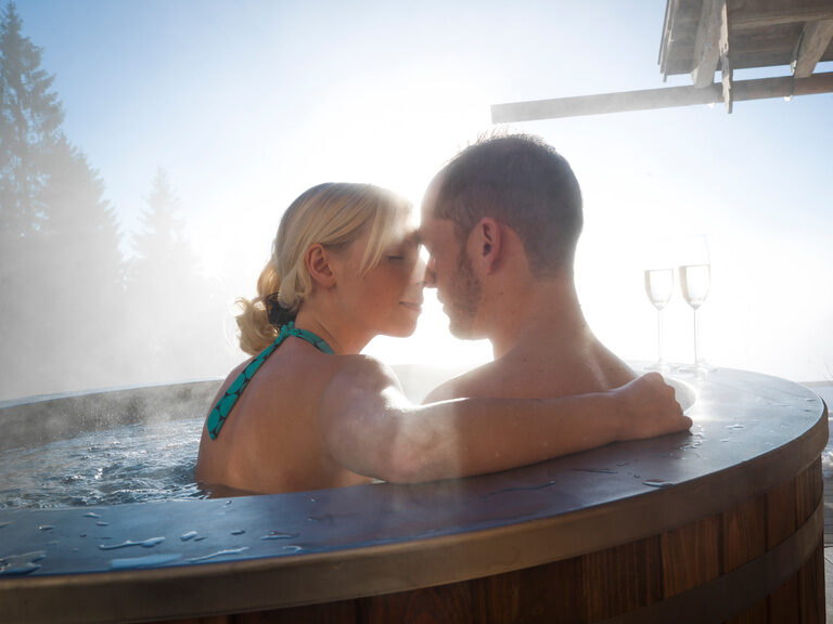 Blauer beleuchteter Außenpool vom Wellnesshotel Hüttenhof Blauer, beleuchteter Außenpool, umgeben von Liegen und Sonnenschirmen auf grüner Wiese