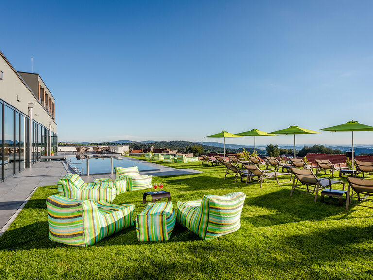Außenpool mit Panorama auf Bayerischen Wald, umgeben von Wiese mit Liegen und Sonnenschirmen Außenpool mit Panorama, umgeben von Wiese mit Liegen und Sonnenschirmen