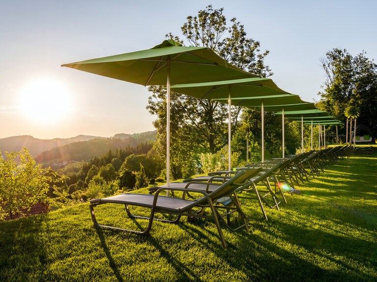 Sonne strahlt auf Außenbereich mit Liegen vom Luxushotel Hüttenhof Sonniger Außenbereich des Hotel Hüttenhof mit Liegen und Schirmen auf Wiese
