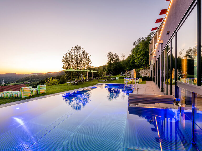 Beleuchteter Außenpool bei Dämmerung mit Gartenbereich vor Luxushotel Hüttenhof