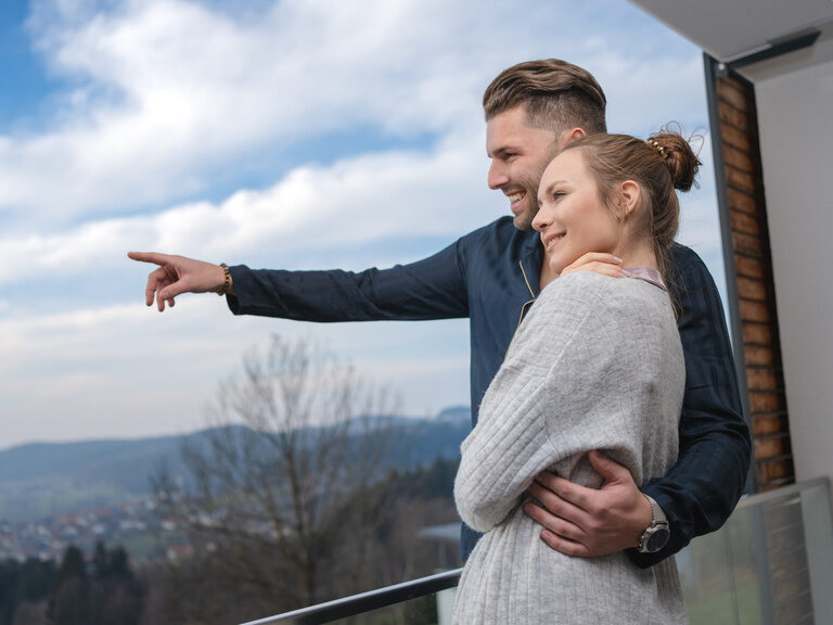 Arm in Arm stehendes Liebespaar schaut in die Ferne des 4 Sterne Wellnesshotel Hüttenhof in Bayern