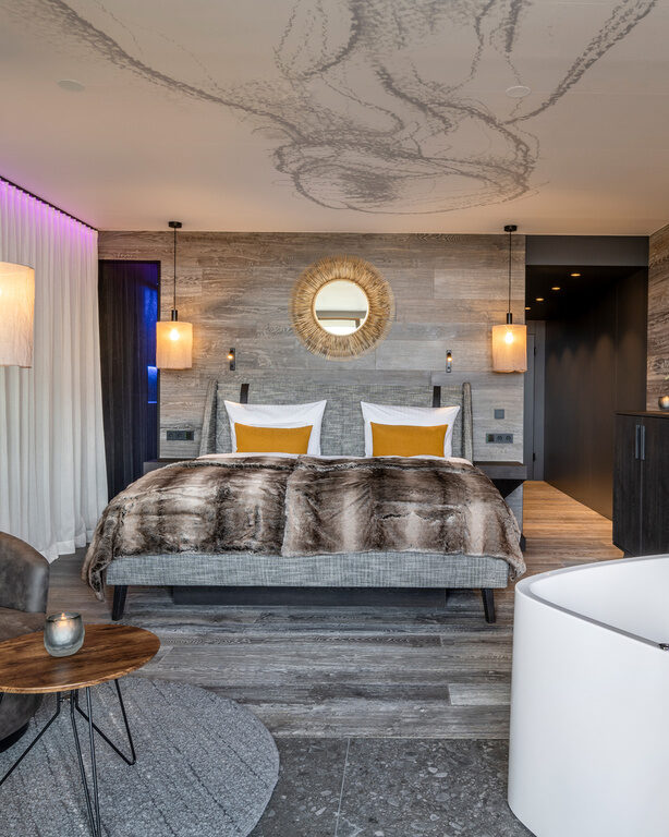 Modernes Hotelzimmer mit Holzwänden, Doppelbett, frei stehender Badewanne und Ledersessel