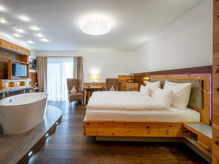 Modernes Hotelzimmer mit Holzelementen, offener Badewanne, Sitzecke und großem Doppelbett