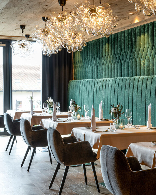 Modernes Restaurant mit Kronleuchtern und grüner Samtbank im 4-Sterne-Hotel Hüttenhof