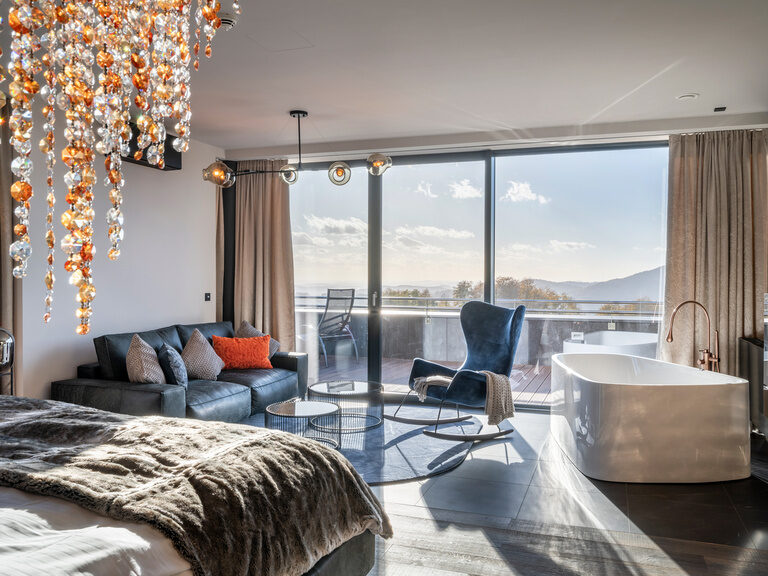 Offene Badewanne und Samt-Sofa in Luxuszimmer mit sonnigem Balkonausblick