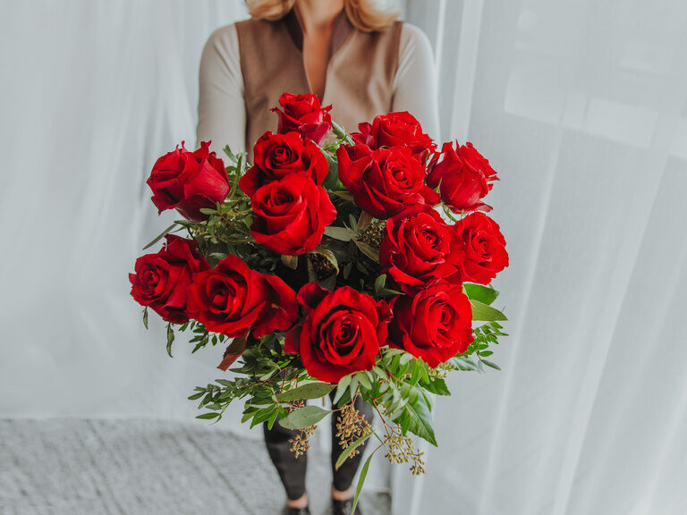 Rosenstrauß in Glasvase auf Beistelltisch vor Stoffsessel im Luxushotel Hüttenhof Rosenstrauß in Glasvase auf rundem Beistelltisch, Stoffsessel und rundes Bett im Hintergrund