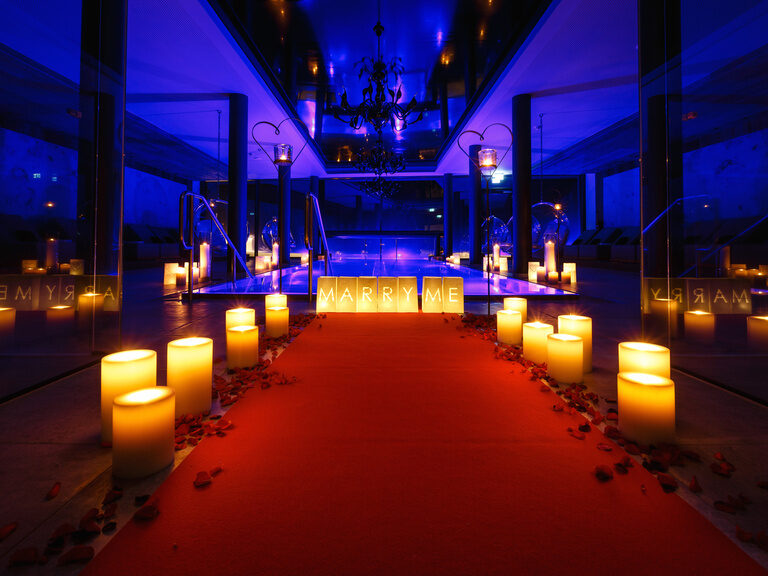 Roter Teppich, an der Seite Kerzen, führt zu beleuchteten Innenpool und Leuchtschrift 'Marry Me'