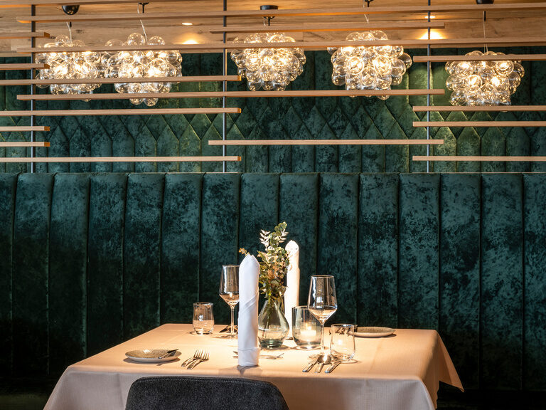 Eingedeckter Tisch in edlem Restaurant mit grüner Samtbank im Hüttenhof