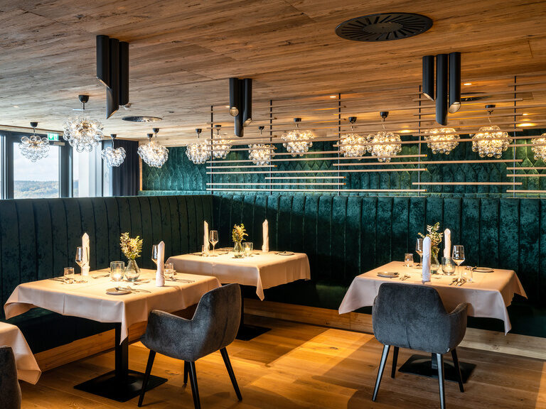 Elegantes Restaurant mit Holzdecke, Kronleuchtern und grünen Samtbänken