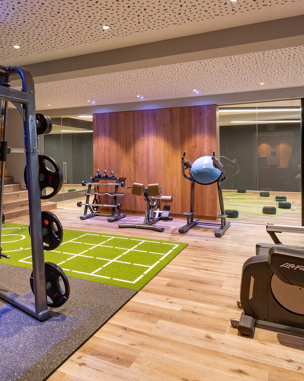 Moderner Fitnessraum im Hüttenhof mit Trainingsgeräten, Glasabtrennung, Spiegelwand und Holzboden