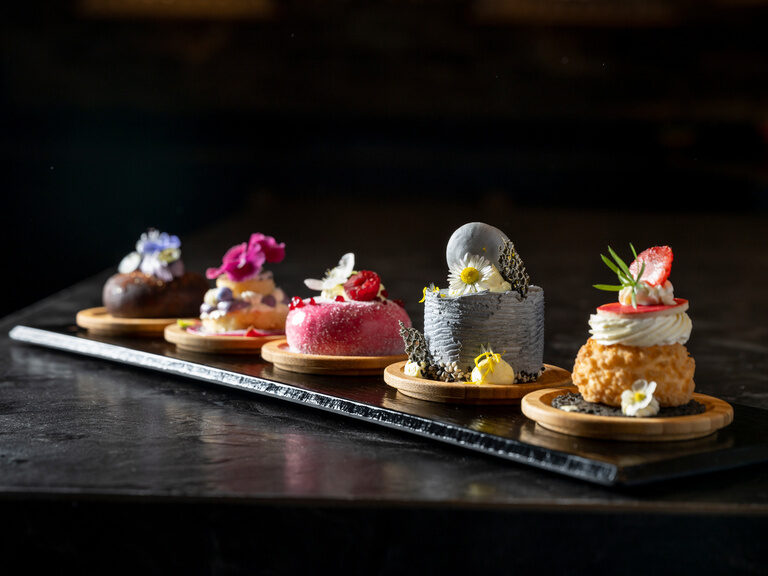 Fünf kleine bunte Dessert-Variationen auf rechteckiger Platte mit Blumenverzierung