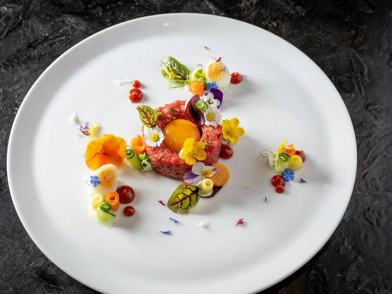 Exotisches Gericht mit Ei und Blumenverzierung auf rundem Teller auf Steinplatte