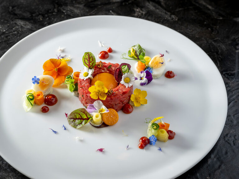Exotisches Gericht mit Ei und feiner Blumenverzierung auf rundem Teller auf Steinplatte