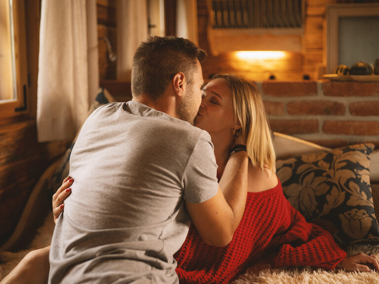 Liebespaar, küsst sich liebevoll auf gemütlichen Sofa in rustikalen Holz-Hütte