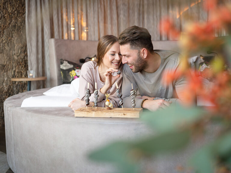 Glückliches Pärchen liegt im Bett und schnabuliert Schokofrüchte des 4 Sterne Luxushotel Hüttenhof im Bayerischen Wald Glückliches Pärchen liegt im Bett und schnabuliert Schokofrüchte im 4 Sterne Luxushotel Hüttenhof im Bayerischen Wald