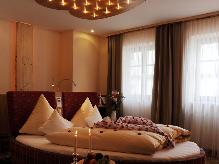 Herzförmiges Bett, dekoriert mit Blütenblättern und Kerzen, daneben ein Obstteller