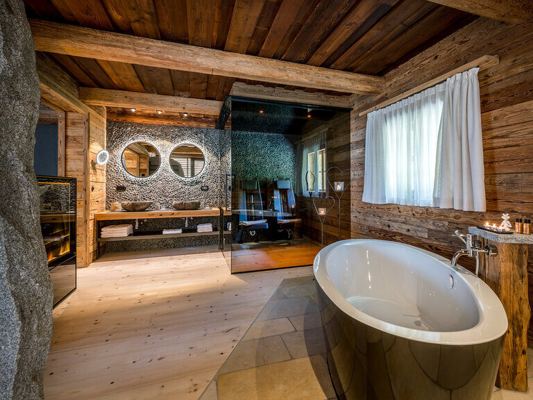 Modernes Badezimmer mit Holzwaschtisch, zwei Waschbecken, beleuchteter Dusche, davor rundes Doppelbett