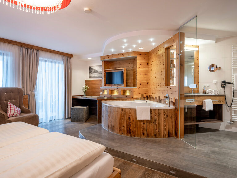 Modernes Badezimmer in Hotelzimmer mit offener Holz-Badewanne, darüber Flachbild-TV