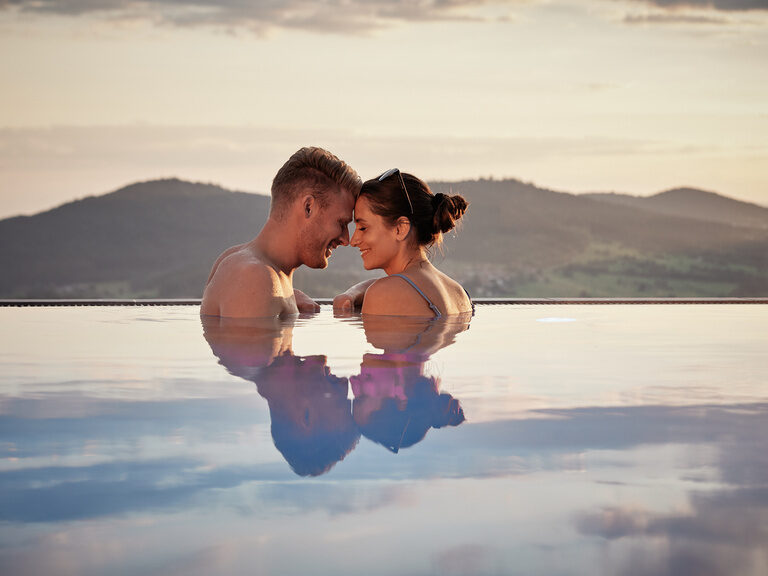 Lächelndes Paar genießt Panorama im Außenpool vom 4-Sterne-Luxushotel Hüttenhof