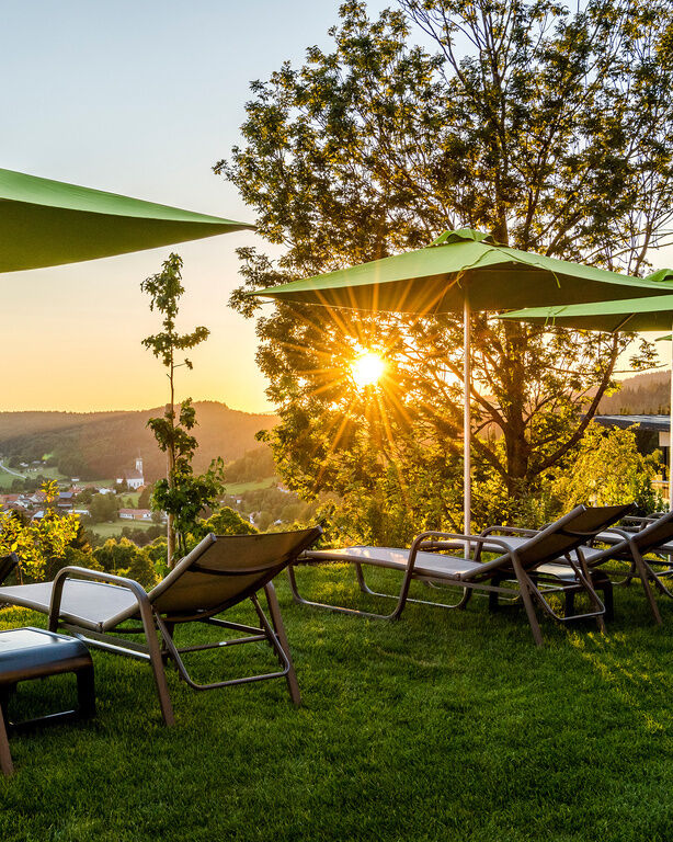Liegen und Sonnenschirme im sonnenbeschienenen Garten, mit Blick auf den Bayerischen Wald
