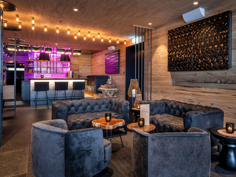 Loungebereich mit vier Sofas vor moderner Bar mit violetter Beleuchtung