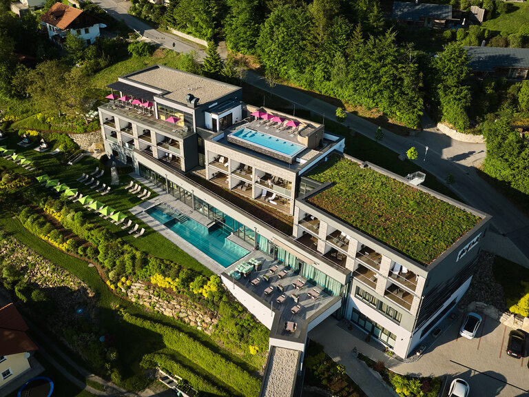 Luftaufnahme des Luxushotels Hüttenhof mit Dach- und Außenpool, umgeben von Wald