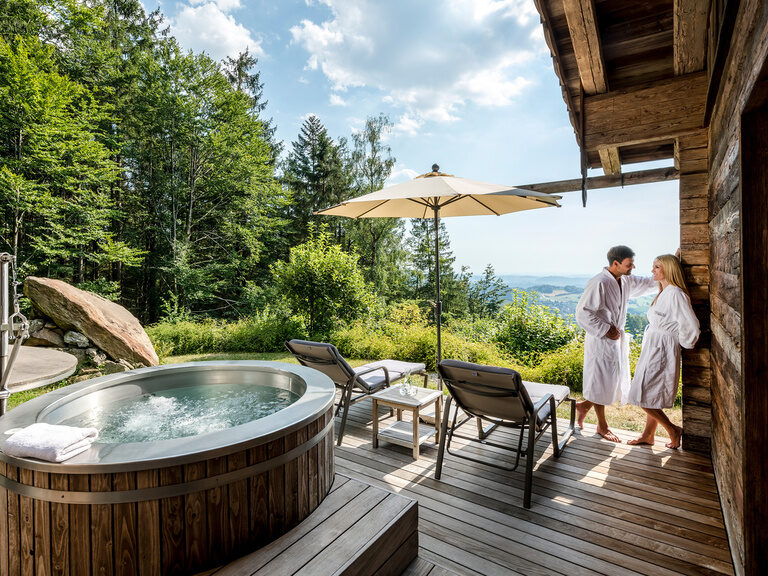 Pärchen im privaten Wellnessbereich mit Liegen, Sonnenschirm, Whirlpool und Aussicht über Bayern