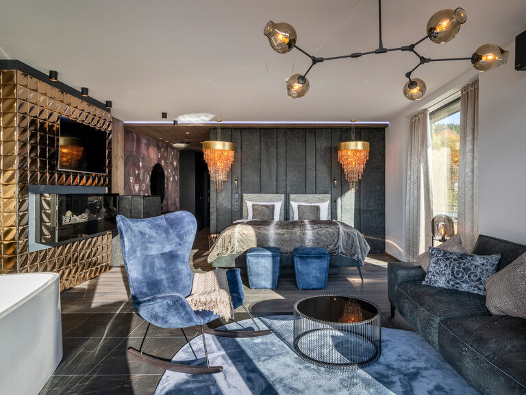 Modernes Luxuszimmer im 4-Sterne-Wellnesshotel Hüttenhof Luxuszimmer im Wellnesshotel Hüttenhof mit goldenem Kamin, Sofa und Bett