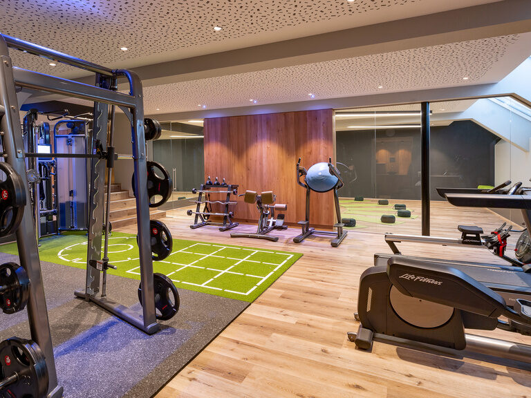 Moderner Fitnessraum mit Glaswand und Geräten im Wellnesshotel Hüttenhof Modern ausgestatteter Fitnessraum mit Glaswand und Trainingsgeräten im Hüttenhof