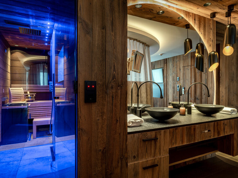 Modernes Bad mit runden Waschbecken, Holzwaschtisch, großem Spiegel und beleuchteter Sauna