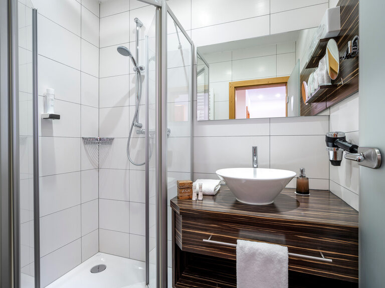 Modernes Bad mit Waschbecken auf Holzregal, darüber Spiegel, daneben Dusche