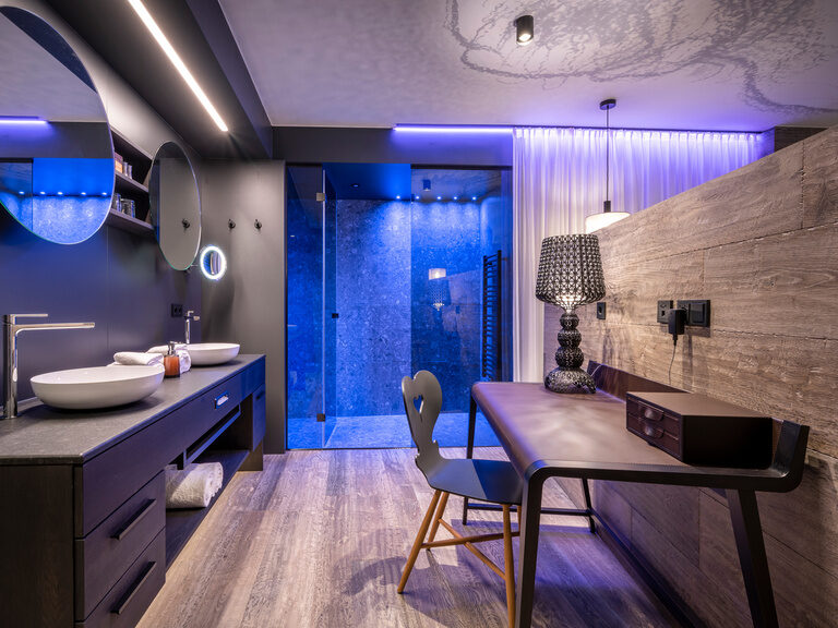 Modernes Badezimmer mit dunkler Einrichtung, beleuchteter Dusche und Sitzgelegenheit