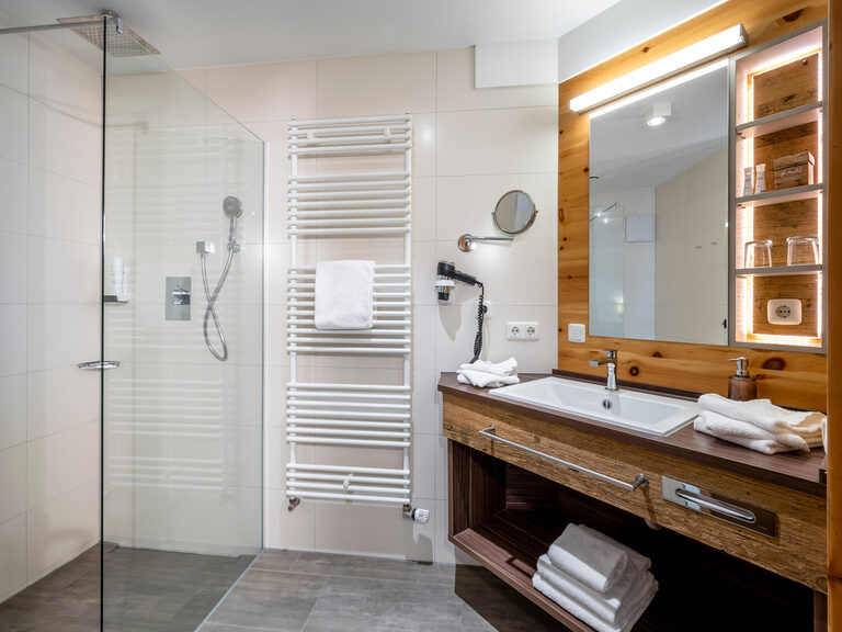 Modernes Badezimmer mit beleuchtetem, hölzernem Waschschrank, Kosmetikspiegel und Dusche