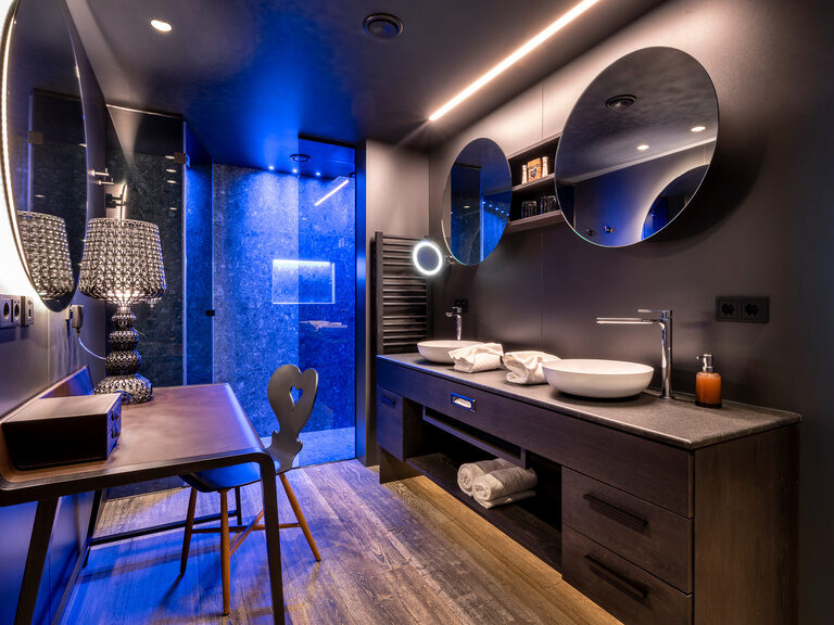 Modernes, dunkles Badezimmer mit runden Spiegeln und bunt beleuchteter Dusche