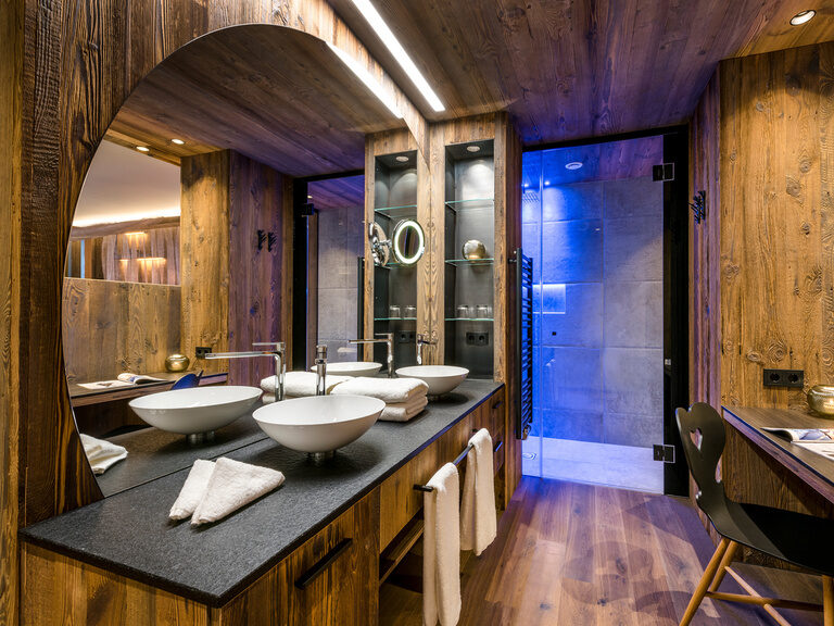 Modernes Badezimmer mit Holzwänden, runden Waschbecken, großem Spiegel und bunt beleuchteter Dusche