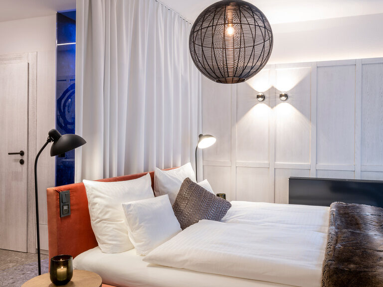 Modernes Doppelbett in hellem, modernem Hotelzimmer, daneben hölzernem Nachttisch