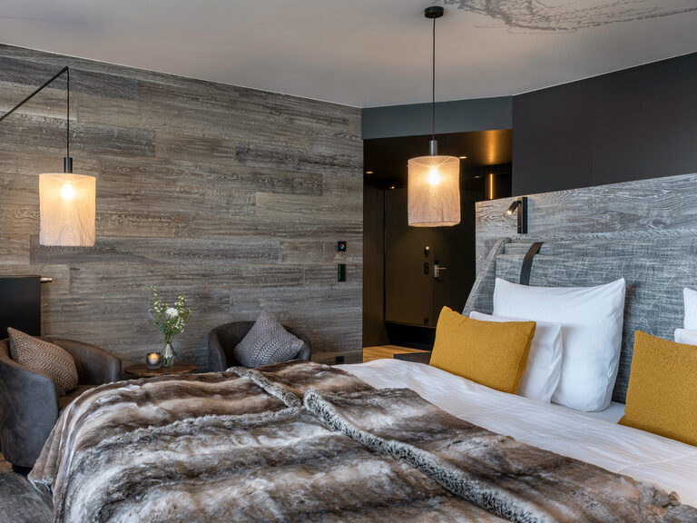 Modernes Doppelbett mit Felloptik-Überwurfdecke, daneben zwei Sessel, Beistelltisch und Stehlampe